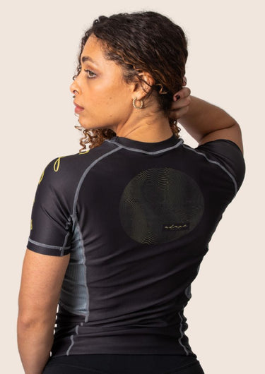 Women’s technical BJJ rashguard in black and gold, featuring four‑way stretch and mesh ventilation.