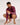 A man wearing a tight-fitting maroon long-sleeve rash guard and matching shorts, crouching in a studio setting and pointing to the script logo on his sleeve.