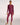 A woman modelling a matching long-sleeve rashguard and full-length leggings set in a maroon color, standing against a plain white studio background.