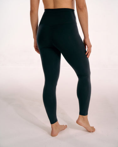 A model from behind wearing high-waisted black leggings, standing barefoot against a plain white studio background.