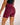A close-up back view of a model wearing high-waisted athletic shorts in a maroon colour, paired with a black sports bra, against a plain light background.