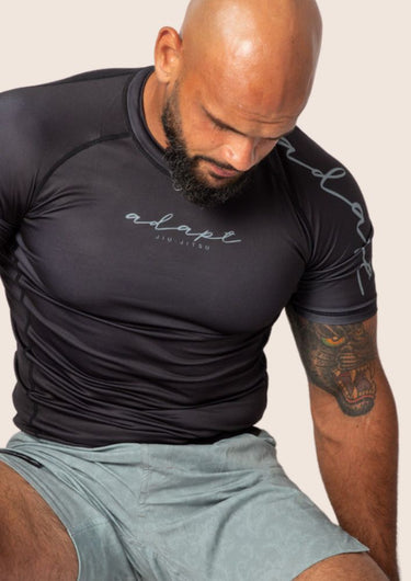 An adult male wearing a black rashguard with the brand 'Adapt' visible on the clothing.