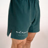 Dark teal green BJJ shorts with a side slit and white 'adapt JIU-JITSU' logo on the lower left leg, shown on a model against a light background.