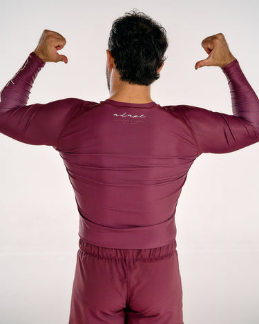 A man viewed from behind wearing a matching maroon long-sleeve athletic top and shorts set, posing with his arms raised in a flexing gesture against a plain white studio background.