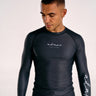 A man wearing a black long-sleeve BJJ rashguard with white script branding on the chest and sleeve, photographed against a plain light background.