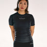 A woman modelling a black short-sleeve BJJ rashguard and matching black leggings with the 'adapt' brand logo, shot against a plain light background.