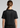 A woman viewed from the back wearing a black short-sleeve crop top T-shirt with white printed text reading 'ADAPT JIU-JITSU' and 'ESTD LONDON 2018' on the upper back.