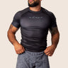 A man wearing a black Adapt Classic Rashguard with short sleeves and paired with gray paisley shorts.